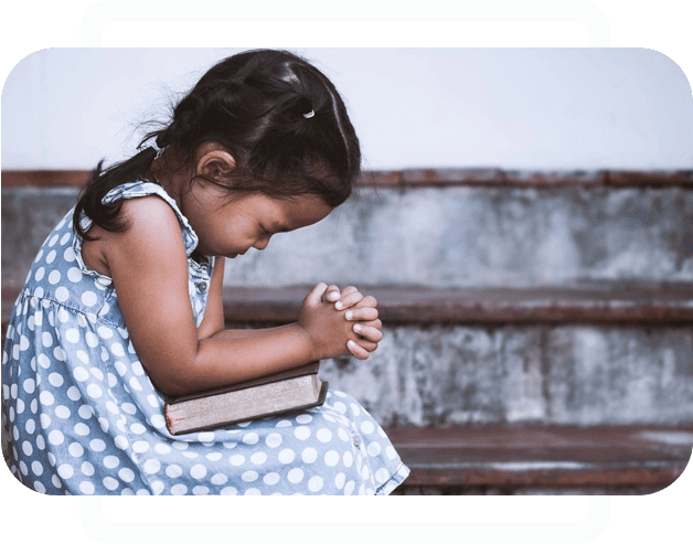 A little girl sitting on the ground with her hands folded in front of her chest.