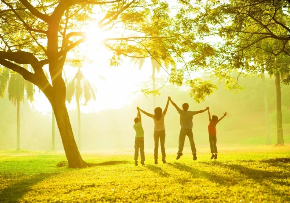 A group of people standing under a tree with their arms in the air.