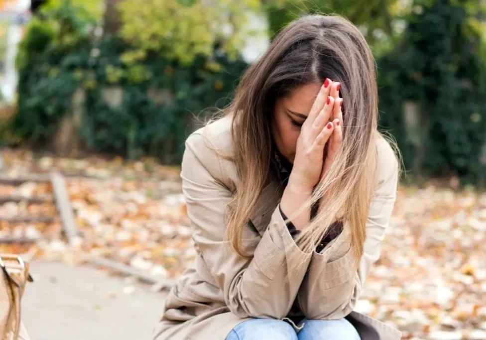 A woman sitting on the ground with her hands in front of her face.